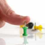 A man's thumb pressing against the pointy end of a thumbtack